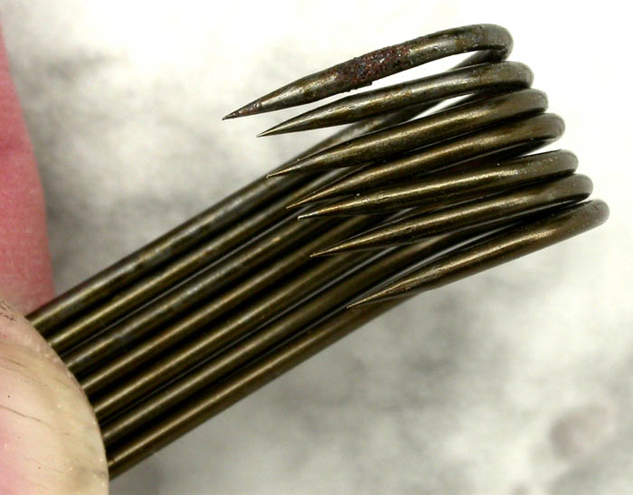 Seven unidentified, marked shank, about 2/0, kirbed, bronzed hooks. These hooks have distinct signs of hand worked hooks. The marks are all over the place including on the sides of the shanks which is seldom seen and the kerbing is uneven. You can see the hooks lined up in the lower photo, the wires should all be touching. They do not.